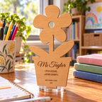 Personalised wooden flower-pot teacher plaque with clear acrylic stand on a sunlit classroom desk. Digital lifestyle visualisation; books, stationery and other styling props are not included.