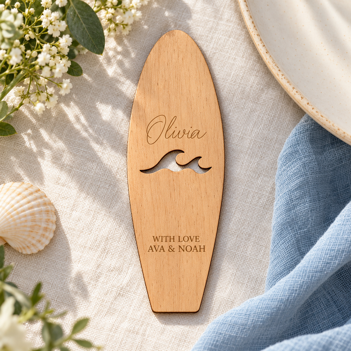 Digital lifestyle visualisation of the personalised Olivia wooden surfboard place card with wave cut-out, lying on wedding table linen; stand not shown.