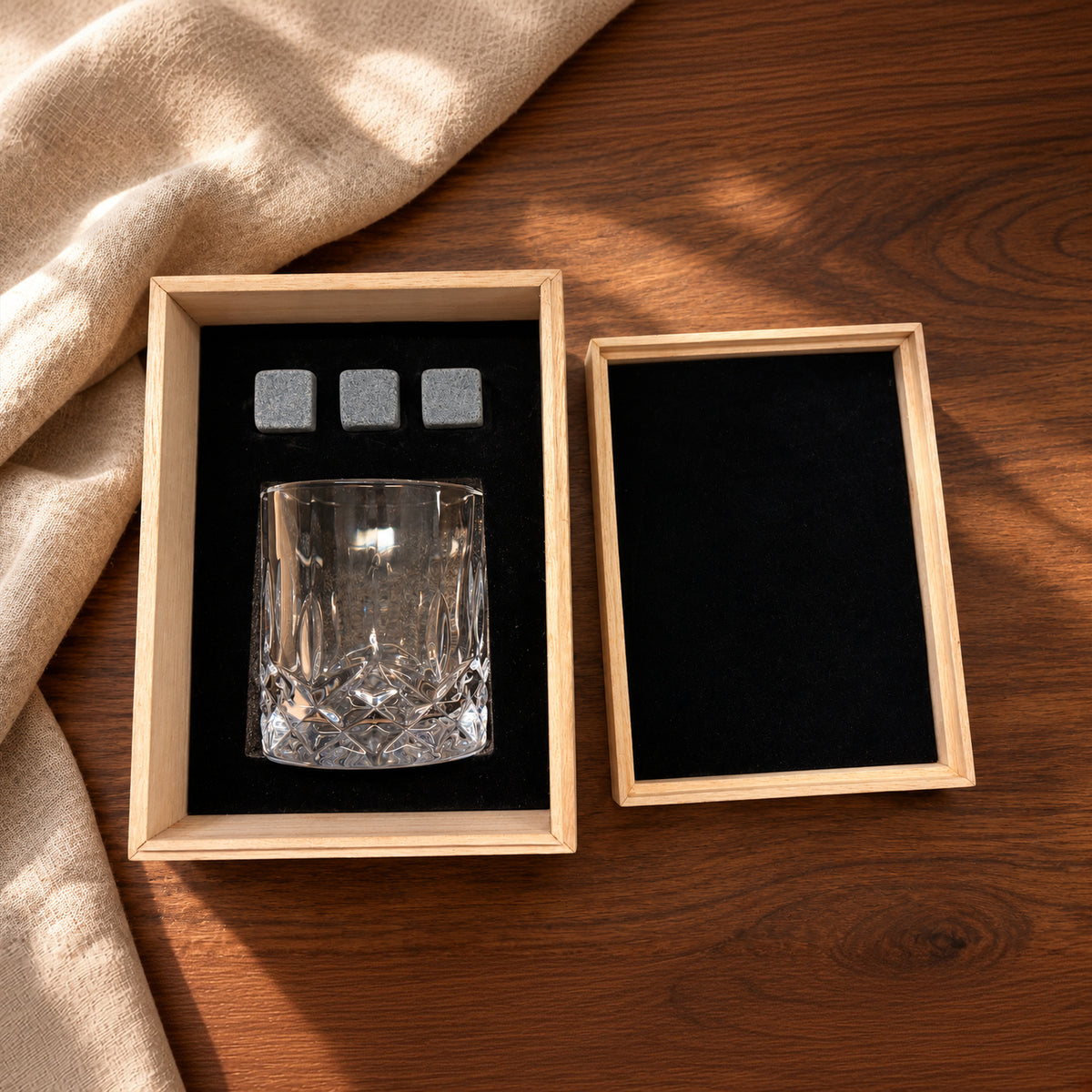 One whisky glass and three grey stones in a pale wooden gift box; lifestyle styling